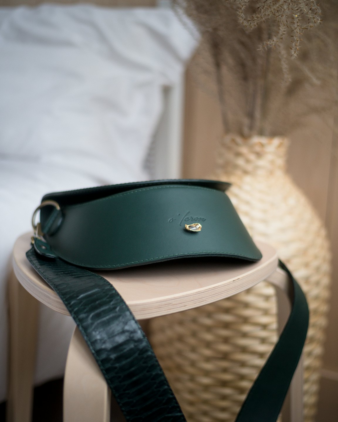 Dark green leather handbag on a wooden stool.