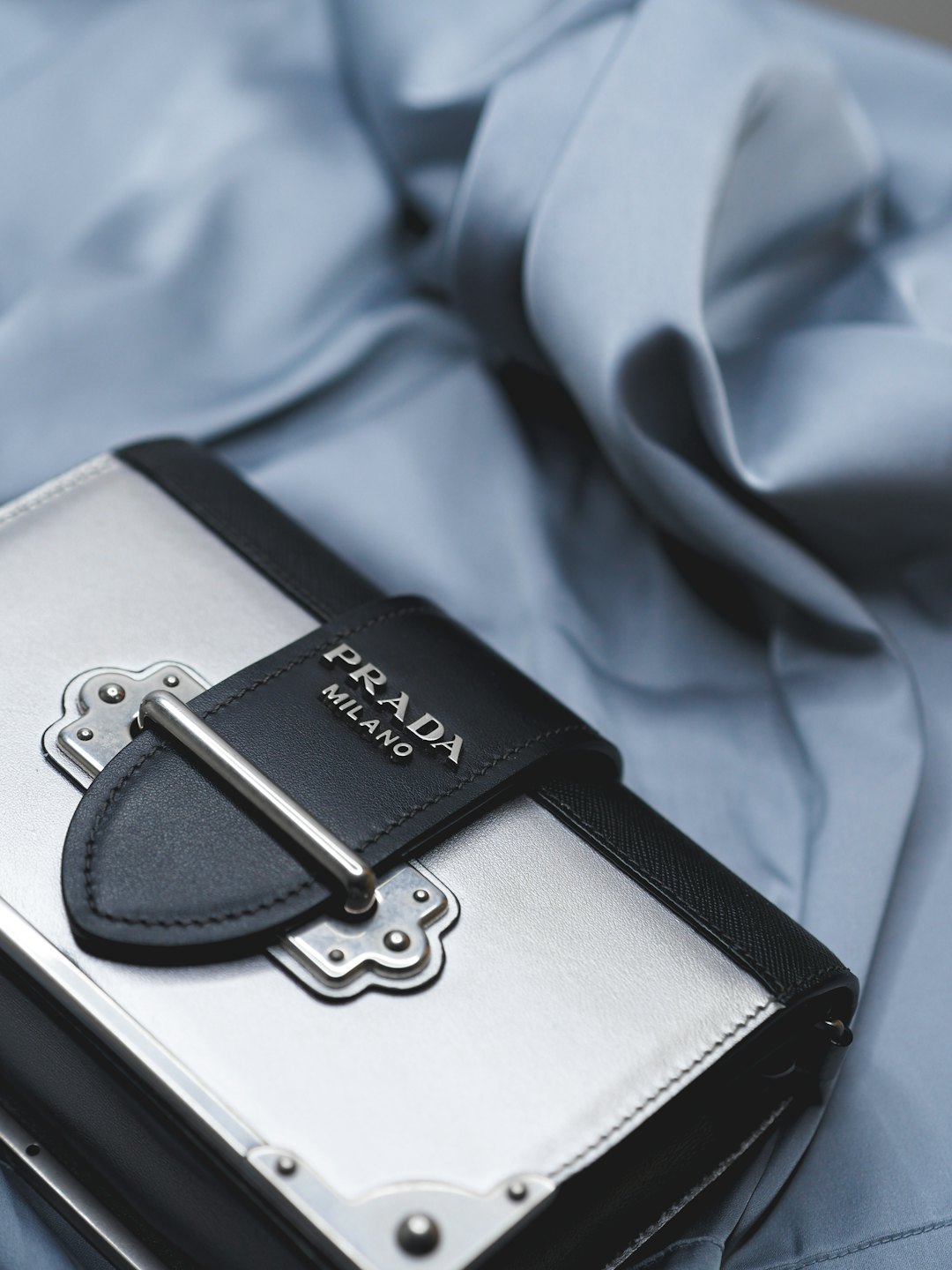 Silver designer handbag with black leather accents on blue fabric.