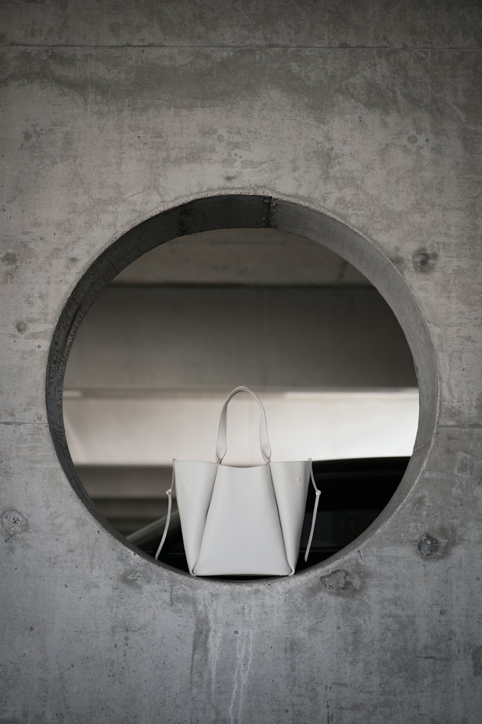 Light grey leather handbag in a circular concrete wall cutout.