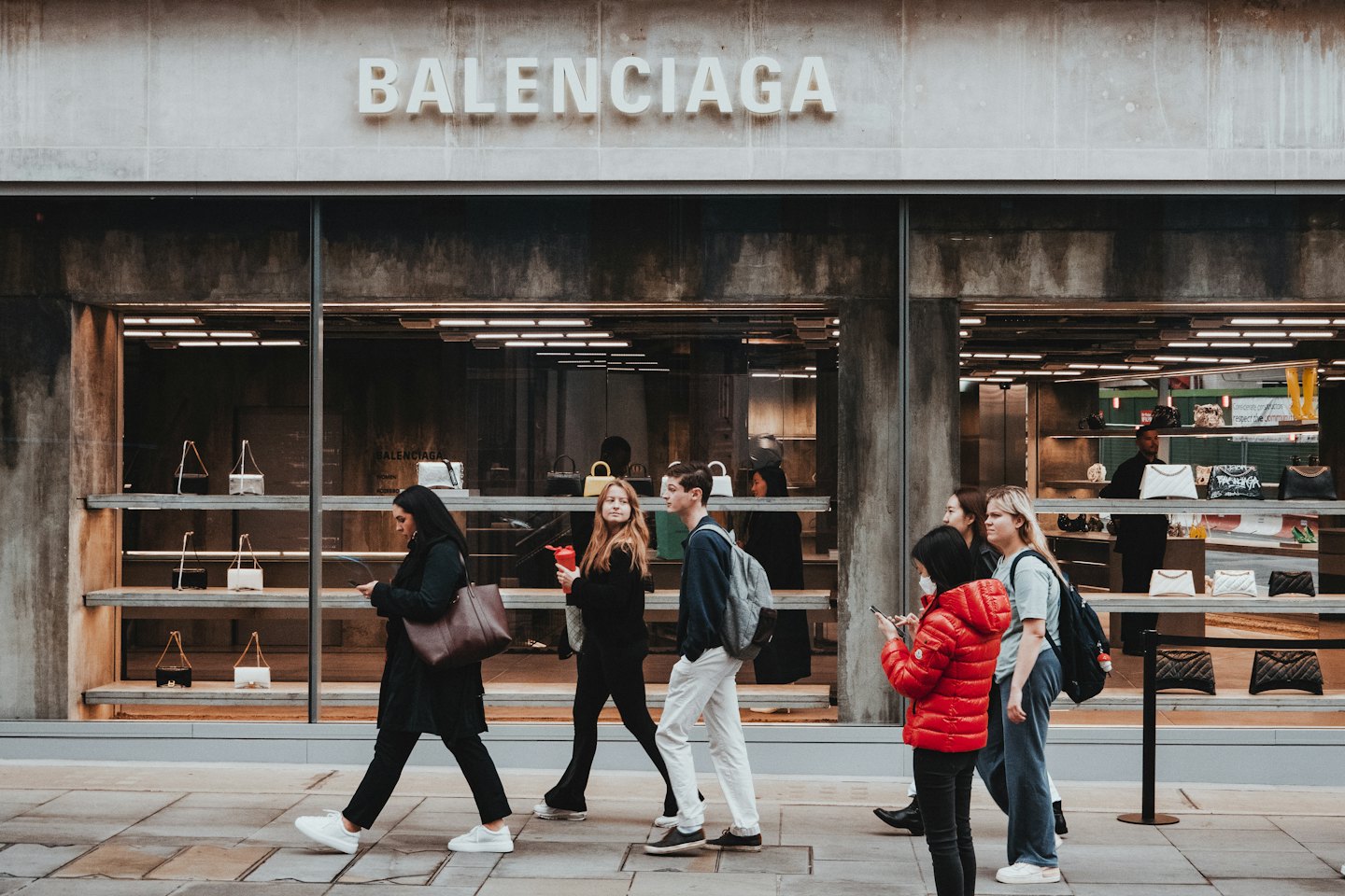 Pedestrians walk past a Balenciaga store on a city sidewalk.